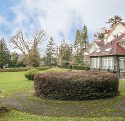 A garden with trimmed bushes and trees beside a large stone and brick house at Lake House Loft in Bowness-On-Windermere