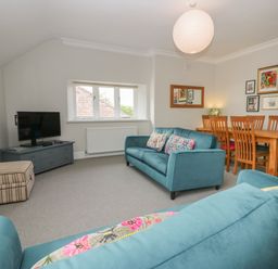 A living room with two blue sofas a wooden dining table with chairs a TV on a blue cabinet and wall art at Lake House Loft in Bowness-On-Windermere