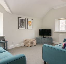 A living room with two teal sofas a striped ottoman a TV on a blue cabinet and two framed pictures on the wall at Lake House Loft in Bowness-On-Windermere