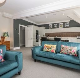 A living room with teal sofas and a kitchen area in the background at Lake House Loft in Bowness-On-Windermere