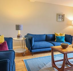 A living room with blue sofas yellow and red cushions a wooden coffee table and lamps at The Wardens House in Tregynon near Newtown