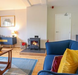 A living room with a blue sofa with cushions a coffee table a wood burning stove and a sideboard at The Wardens House in Tregynon near Newtown
