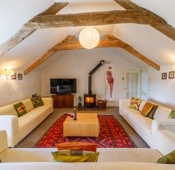 A living room with white sofas a red patterned rug wooden beams and a wood burning stove at Aarons Cottage in St Teath