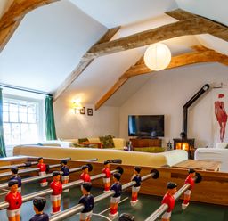 A room with a foosball table in front of sofas a wood burning stove and a television at Aarons Cottage in St Teath