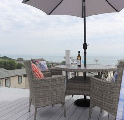 An outdoor deck with a round table and four chairs under an umbrella overlooking the sea at The Retreat in Otterton