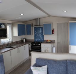 A kitchen with blue and white cabinets a stove and a sink next to a blue sofa at The Retreat in Otterton
