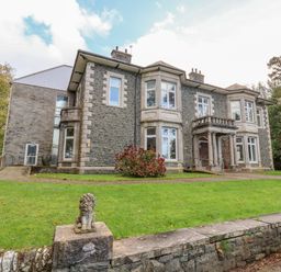 A large stone building with multiple windows and columns surrounded by grass and trees at The Lloyd George in Bontnewydd Gwynedd