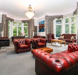 A living room with red leather sofas brown wooden coffee tables and large windows with checkered curtains at The Lloyd George in Bontnewydd Gwynedd