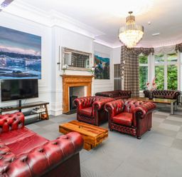 A sitting room with red leather sofas a wooden coffee table large windows with curtains and a chandelier at The Lloyd George in Bontnewydd Gwynedd