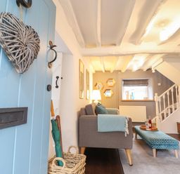 A living room with a blue door wicker heart hanging sofa and ottoman near staircase and TV at 3 Ivy Court in Dolgellau