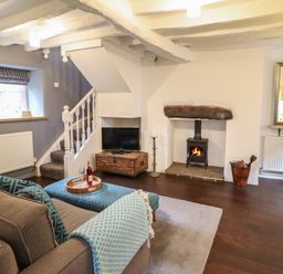 A living room with a gray sofa blue patterned cushions a wood stove and a TV under stairs at 3 Ivy Court in Dolgellau