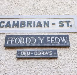 Three street signs on a wall showing Cambrian St Ffordd Y Fedw and Deu-Ddrws in Barmouth