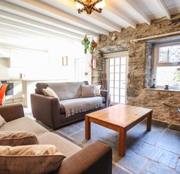 A living room with two sofas a wooden coffee table stone walls and a kitchen area with orange chairs at Deu-Ddrws in Barmouth