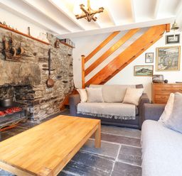 A living room with two sofas a wooden coffee table a stone fireplace and wooden staircase at Deu-Ddrws in Barmouth