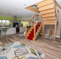 An open kitchen and dining area with a wooden staircase with red carpet and a patterned rug on the floor at Ty Marlyn in Crofty