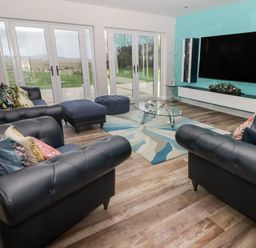 A living room with black leather sofas a glass coffee table large TV and glass doors at Ty Marlyn in Crofty