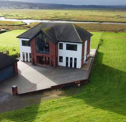 A modern two-story house with a garage and driveway surrounded by green fields at Ty Marlyn in Crofty