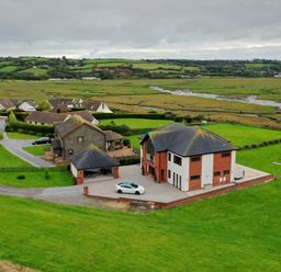A house with a driveway and a car surrounded by green fields and other houses in the background at Ty Marlyn in Crofty