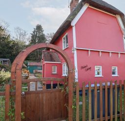 A red cottage with white trim behind a wooden fence and gate at Rhubarb Cottage in Ufford near Woodbridge
