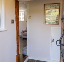 An entryway with a wooden door, a framed map on the wall, and a view into a room with a pink armchair at Rhubarb Cottage in Ufford near Woodbridge