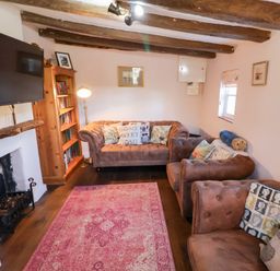 A living room with brown sofas a pink rug a wooden bookshelf and a mounted television at Rhubarb Cottage in Ufford near Woodbridge