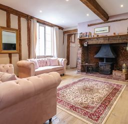 A living room with pink sofas a patterned rug and a fireplace with wooden beams at The Bridewell in Woodbridge