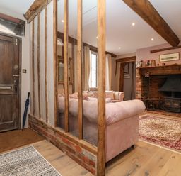 An entryway with a wooden door next to a living room with pink sofas and a fireplace at The Bridewell in Woodbridge