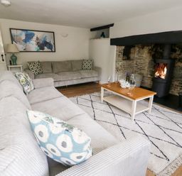 A living room with two sofas a coffee table with glasses and bottle a wood burning stove and a rug at Dairy Cottage in Abbotsbury
