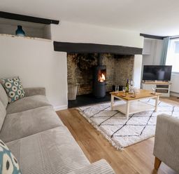A living room with a stove fire a coffee table a TV a sofa and armchair at Dairy Cottage in Abbotsbury