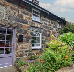 A stone wall with a front door and windows at Riverside Cottage in Beddgelert