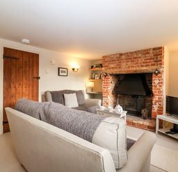 A living room with a brick fireplace two sofas a wooden door and a television at 2 Mosses Cottage in Friston
