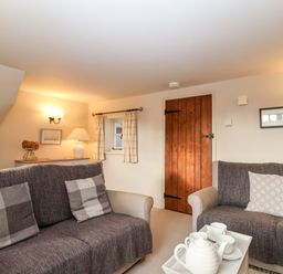 A living room with two sofas a tray with a teapot and cups on a table a wooden door and wall lights at 2 Mosses Cottage in Friston