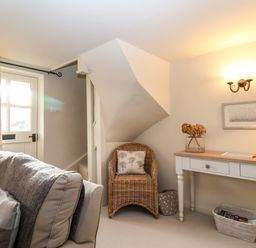 A living room with a sofa a wicker chair a white desk with drawers and a lamp at 2 Mosses Cottage in Friston