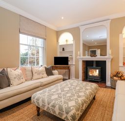 A living room with two sofas a patterned ottoman a fireplace with a wood burning stove and built in shelves at The Middle House in Southwold