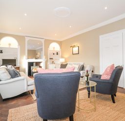 A living room with sofas armchairs a fireplace and a small round table with a wine bottle at The Middle House in Southwold