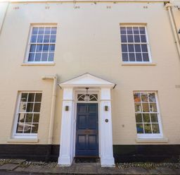 A blue door entrance with white frame and four windows on a beige building at The Middle House in Southwold