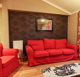 A living room with a red armchair and sofa a patterned rug and a mirror on a dark feature wall at Washburn Lodge in Fewston near Darley