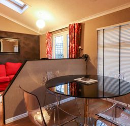 A dining area with a round black glass table and transparent chairs next to a room divider and a red sofa visible beyond the partition at Washburn Lodge in Fewston near Darley