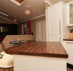 A kitchen area with wooden countertop and white cabinets next to a seating area with a red chair at Washburn Lodge Fewston near Darley