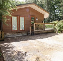 An exterior view of a wooden cabin with two windows and a glass-paneled porch surrounded by trees at Washburn Lodge Fewston near Darley