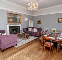 A living room with purple sofas a wooden dining table set with plates and glasses a fireplace and a chandelier at The Stables and West Wing Bolton Percy near Tadcaster