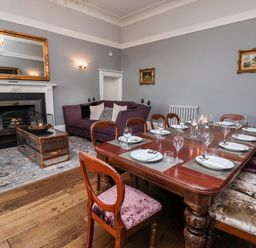 A dining room with a wooden table set for eight people and a purple sofa near a fireplace at The Stables and West Wing in Bolton Percy near Tadcaster