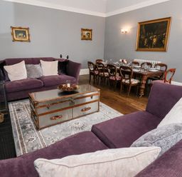 A living room with purple sofas a wooden dining table and framed paintings on gray walls at The Stables and West Wing Bolton Percy near Tadcaster