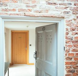 An open white wooden door in a brick wall leading to a hallway with a wooden door at Servant's Quarters Bolton Percy near Tadcaster