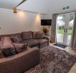 A living room with a sectional sofa a wall-mounted TV and glass doors leading outside at Servant's Quarters Bolton Percy near Tadcaster