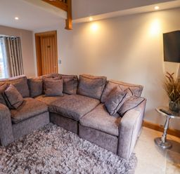A living room with a sectional sofa a shaggy rug a side table with a plant and a wall-mounted TV at Servant's Quarters in Bolton Percy near Tadcaster