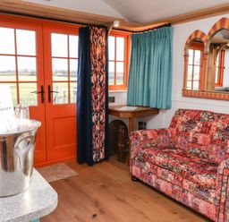 A room with orange framed glass doors curtains a patterned sofa a wooden corner table and a silver ice bucket with bottles at The Storyteller in Bolton Percy near Tadcaster