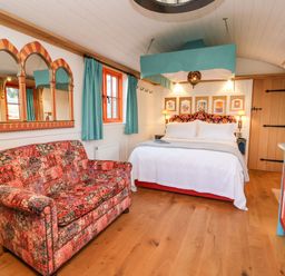 A bedroom with a bed, a patterned sofa, colorful curtains, a mirror on the wall, and a decorated cabinet at The Storyteller in Bolton Percy near Tadcaster
