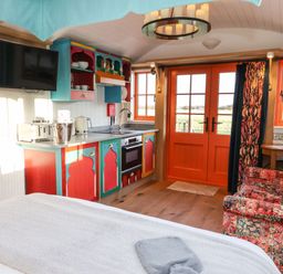 A small living space with colorful kitchen cabinets a mounted television a patterned sofa and orange double doors at The Storyteller in Bolton Percy near Tadcaster