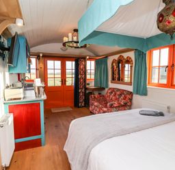 A bedroom with a bed a sofa a kitchen area and orange window frames at The Storyteller in Bolton Percy near Tadcaster